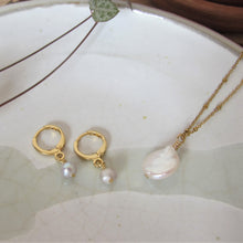 Load image into Gallery viewer, The Full Moon necklace lays besides white pearl earrings on a white background.