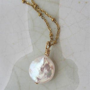 A white round flat keshi pearl hangs on a gold stainless steel chain.
