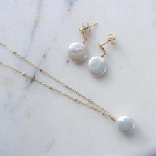 Load image into Gallery viewer, The Full Moon pearl earrings lay besides a matching necklace on a white background.