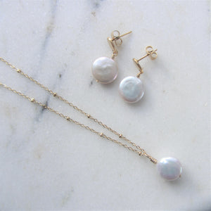 The Full Moon pearl earrings lay besides a matching necklace on a white background.
