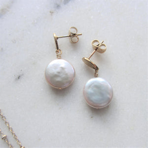 White round flat keshi pearls hang on drop shaped gold earring settings.