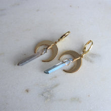 Load image into Gallery viewer, A blue iridescent crystal hangs on gold crescent moon earring settings.