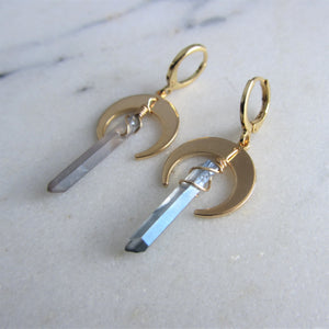 A blue iridescent crystal hangs on gold crescent moon earring settings.